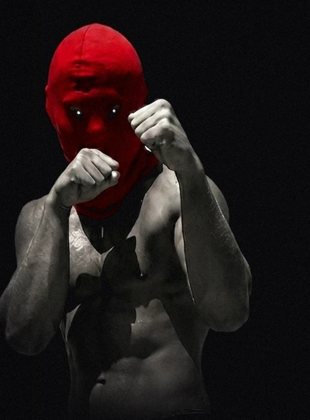 A masked fighter standing in his guard, lit from one side